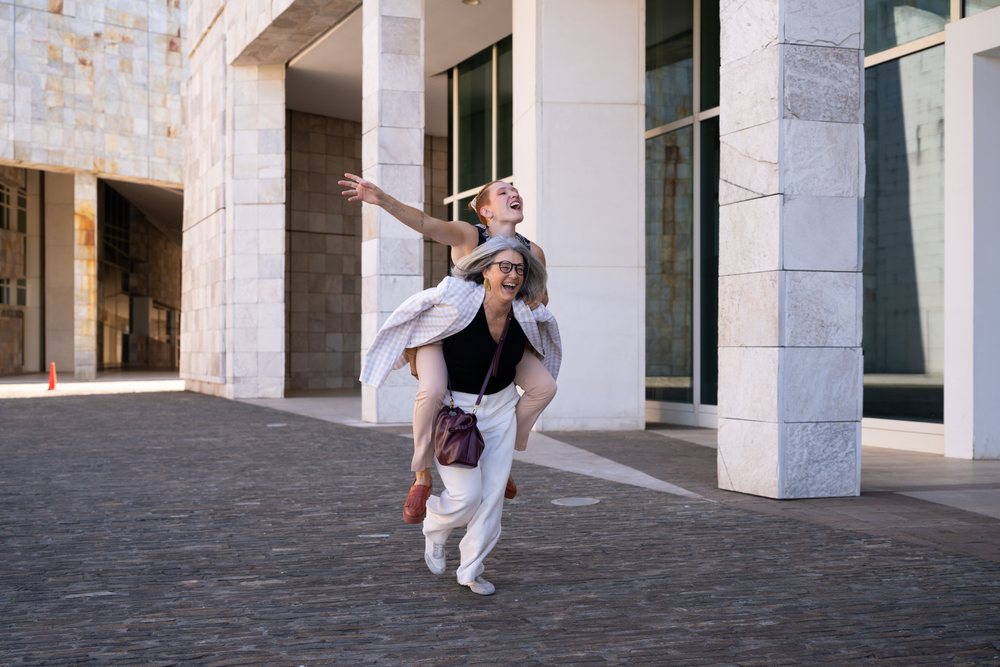 Two women share a joyful piggyback ride on a stone-paved street in urban, businesswomen, Spain.