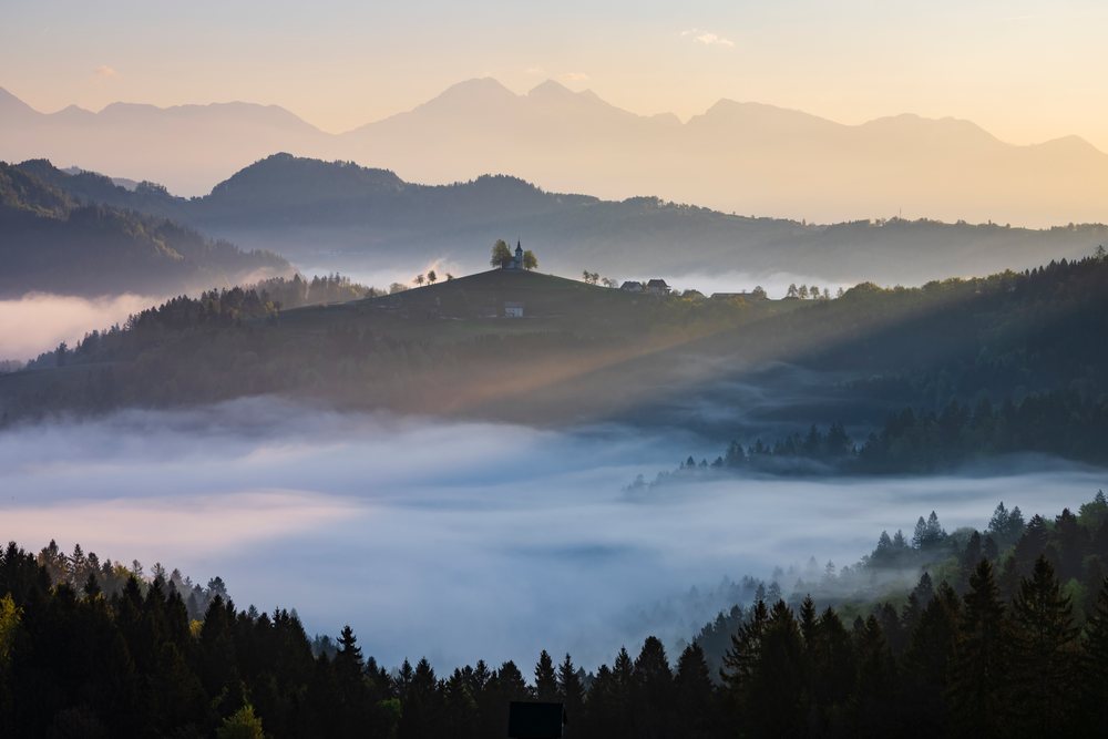 St Thomas's Church atop a hill overlooking misty valleys and mountains at Sunrise, landscape, cityscape, Skofja Loka, Slovenia.