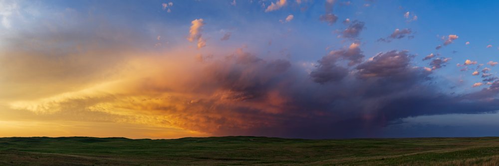 Dramatic storm clouds over rolling grassy hills during a colorful sunset in the Nebraska Sandhills at North Prairie Trace Road, Sutherland, USA.