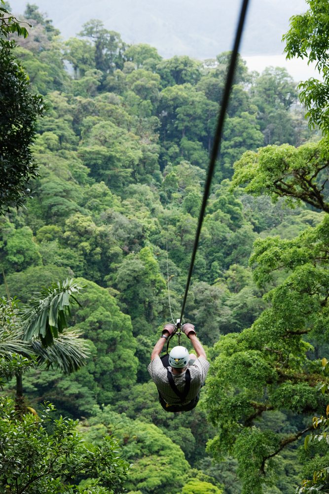 Person wearing helmet and gloves descending on a zip line above dense tropical forest canopy in Costa Rica.