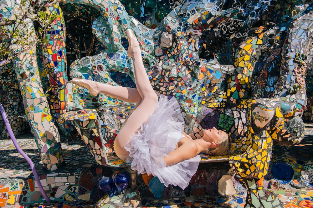Female ballet dancer reclining on a colorful mosaic sculpture bench outdoors under sunlight, CA, USA.