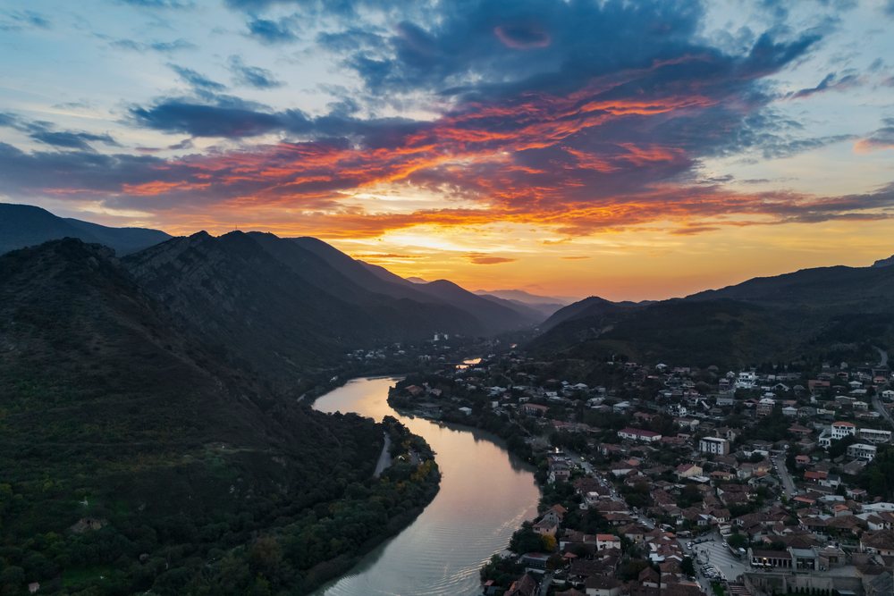 Mtskheta city and the winding Mtkvari (Kura) River flow through mountainous terrain at Sunset under colorful clouds, Georgia.