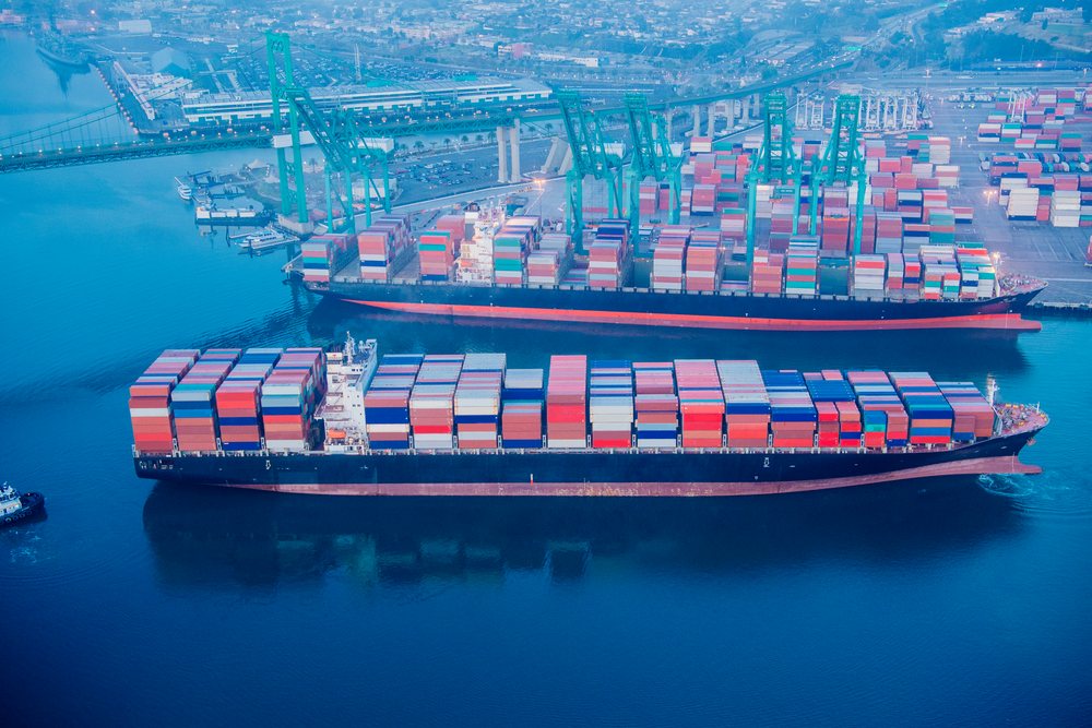 Container ships loaded with colorful shipping containers at a large container terminal with green cranes and waterway visible at the, Port of Long Beach, CA, USA.