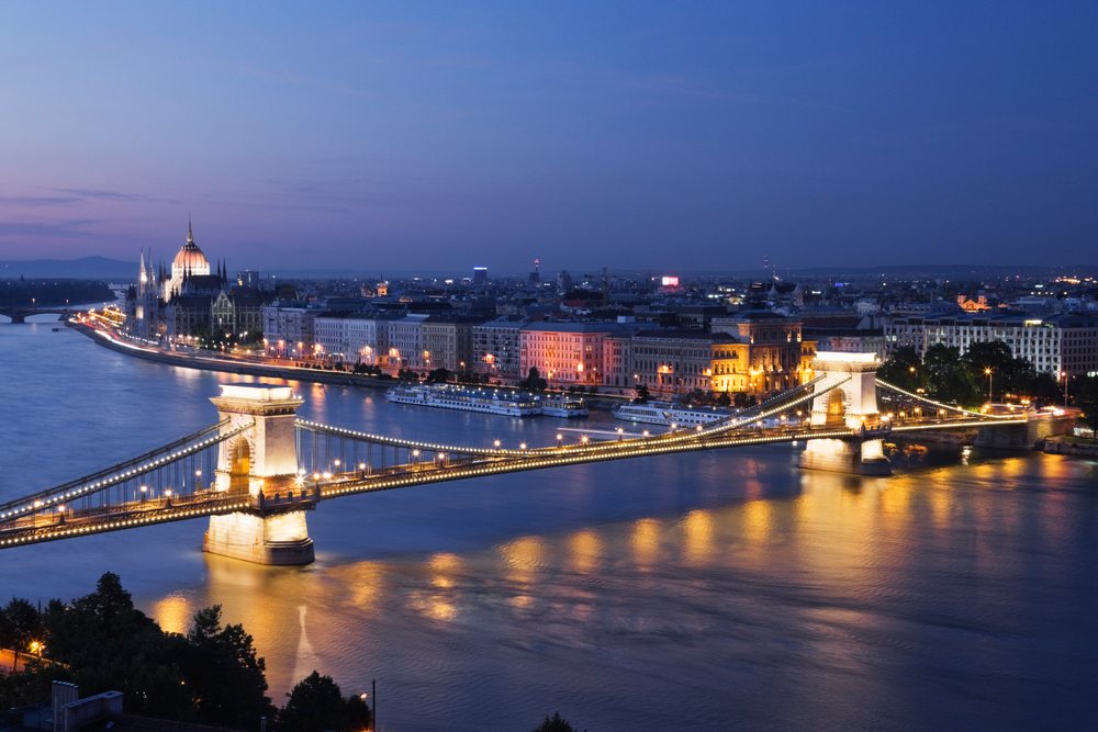 Chain Bridge illuminated at night over the River Danube with Budapest's historic cityscape reflected on calm water, Hungary.