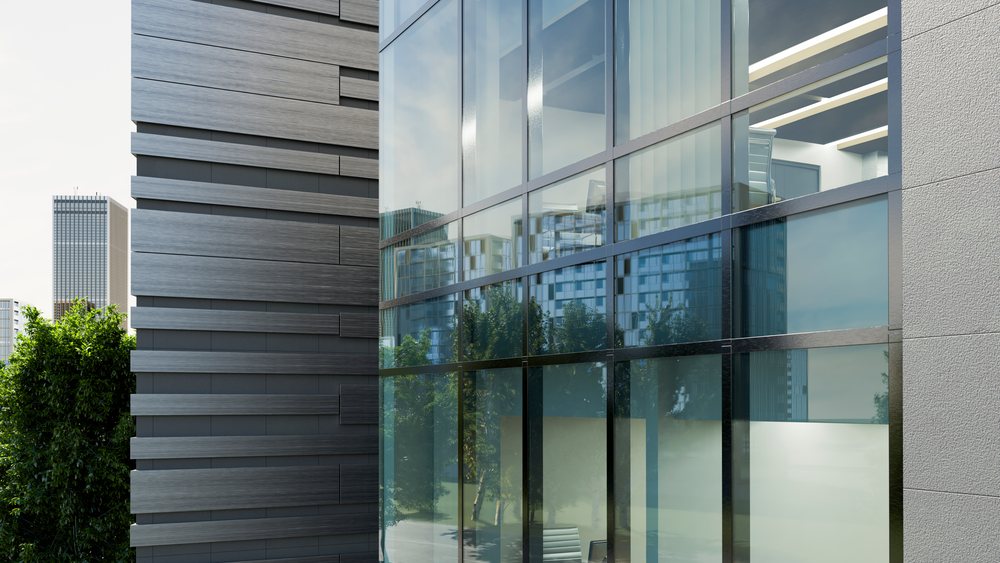 Modern office building with large glass windows reflecting trees and urban cityscape under clear daytime light.