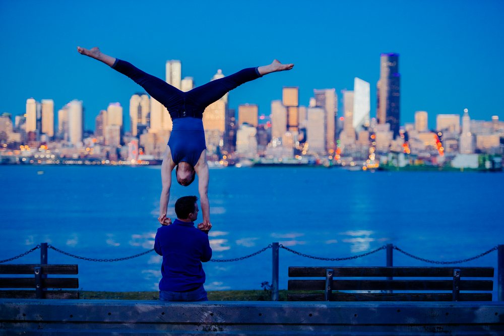 Two men performing partner acrobatics with a handstand near Seattle waterfront at evening light, USA.