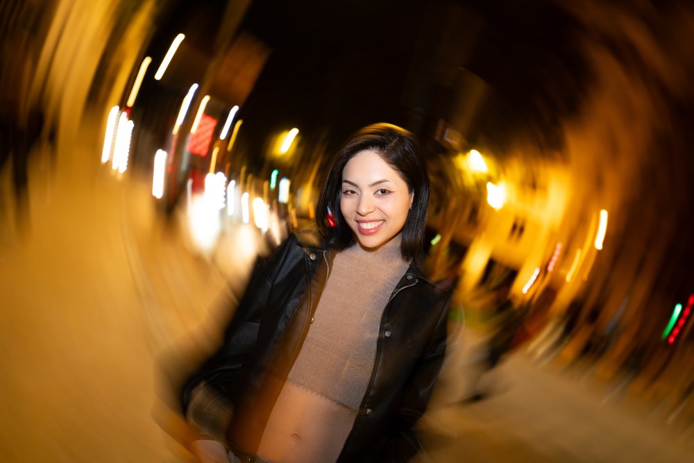 Woman smiles outdoors on a city street at night with visible street lights glowing around her, Madrid, Spain.