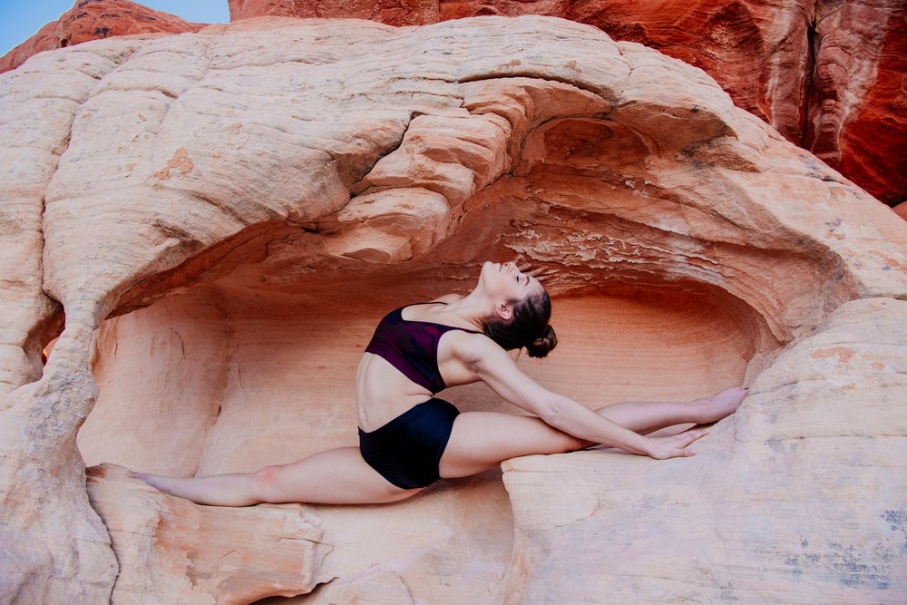 Woman performing an acrobatic yoga split pose on a rock formation outdoors, USA.