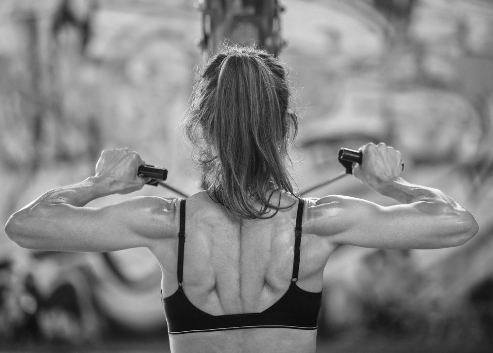 Woman performs a strength training pull exercise using a cable machine in an indoor gym in the USA, showing defined back muscles, Calisthenics.