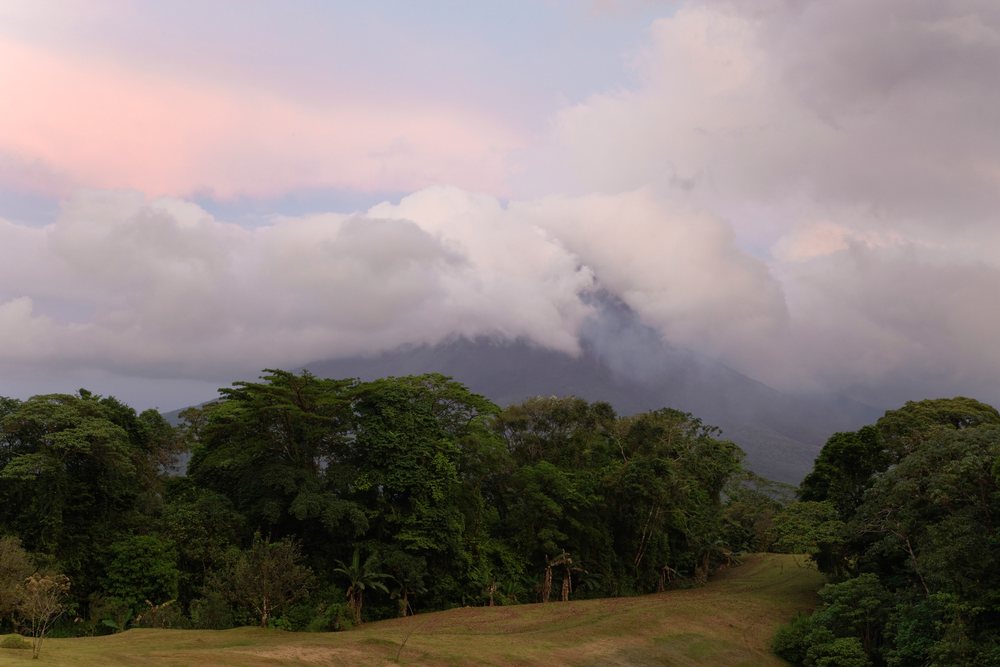 Arenal Volcano emits smoke above clouds and tropical forest's mountain landscape, Costa Rica.