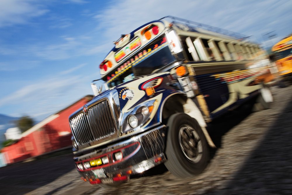 Colorful decorated bus with eagle design moving outdoors on a gravel road, with motion blur effect, Sacatepequez Department, Guatemala.