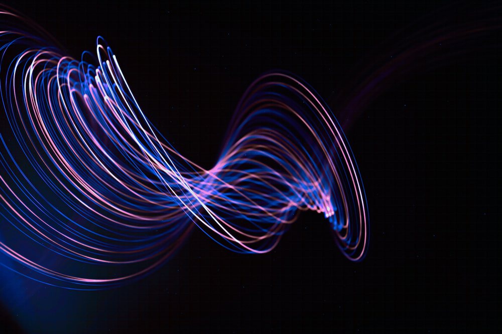 Abstract curved light trails in blue and purple hues create a wave pattern on a dark background.