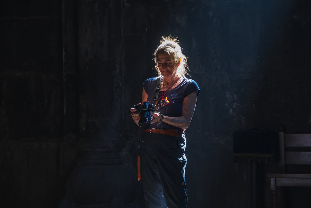 Woman holding a digital camera inside the stone interior of Geghart Monastery in Armenia under a beam of light, Garni, Kotayl Povince.