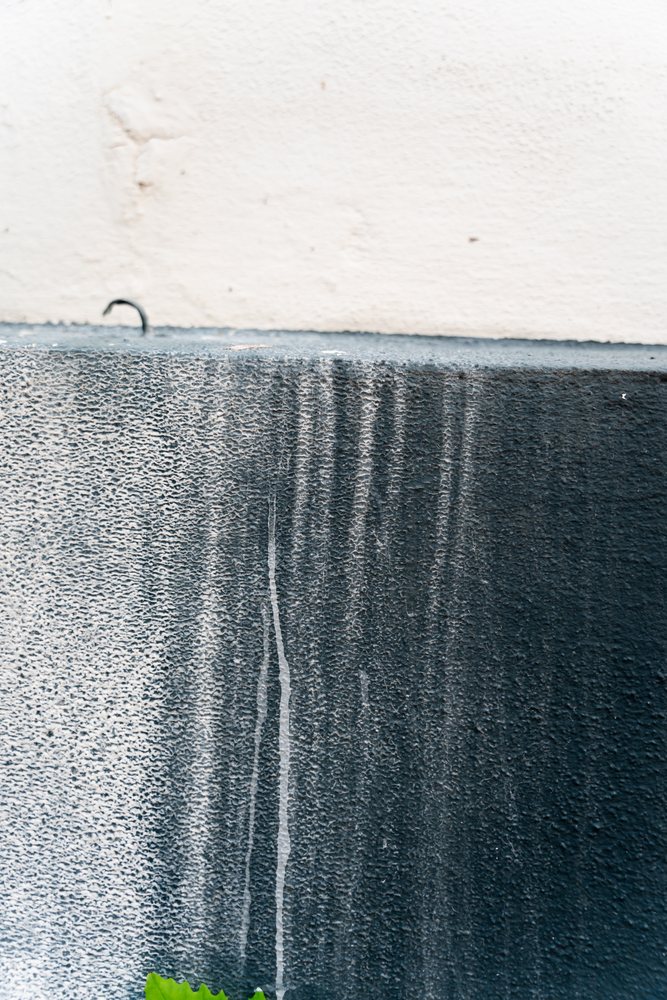 Weathered exterior wall with vertical black and white paint streaks showing rough, flaking texture, abstract texture, background, wallpaper, Spain.