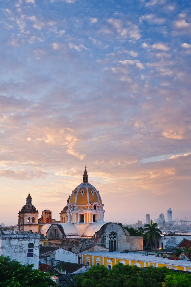 Iglesia de San Pedro Claver church dome and towers at sunset with cityscape and trees, Cartagena, Colombia.