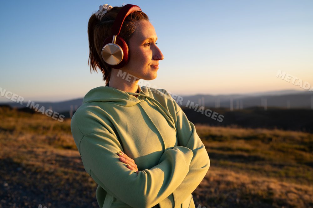 A white woman wearing headphones enjoys the sunset outdoors