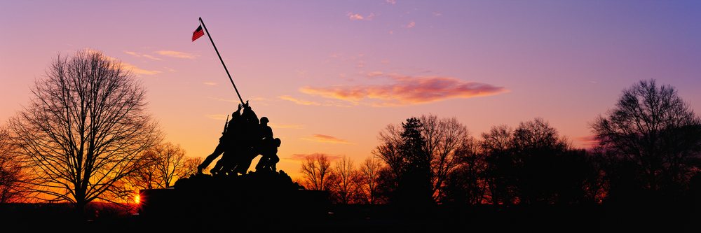 Silhouette of the Iwo Jima Memorial statue at sunset with American flag and surrounding trees, Virginia, USA.