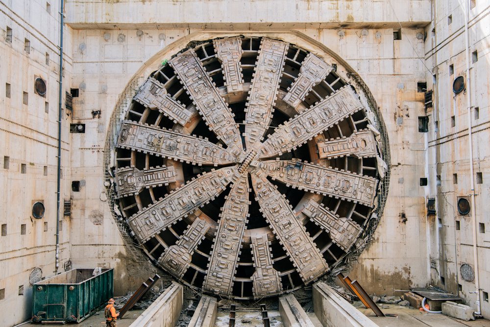 A tunnel boring machine with a worker standing nearby at a construction site, tunnel boring machine, drilling, USA.