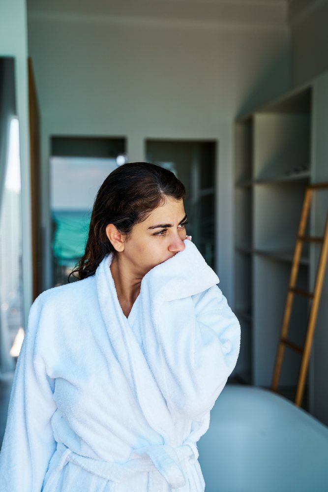 A woman in a white bathrobe looks thoughtfully to the side inside a modern bathroom with a view in the, Maldives.