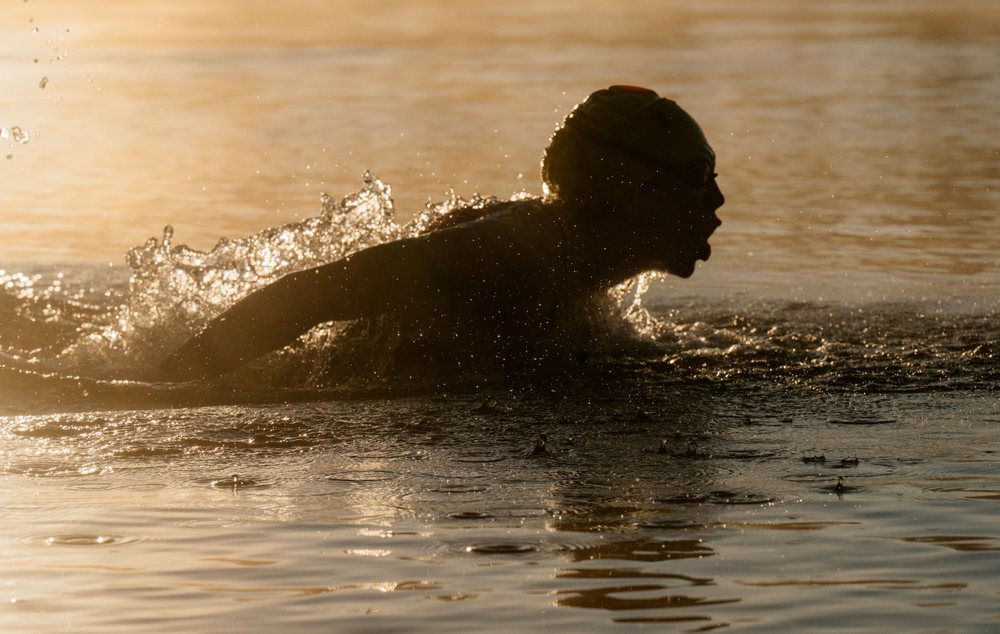 Swimmer performing breaststroke with water splashing during sunset, USA.