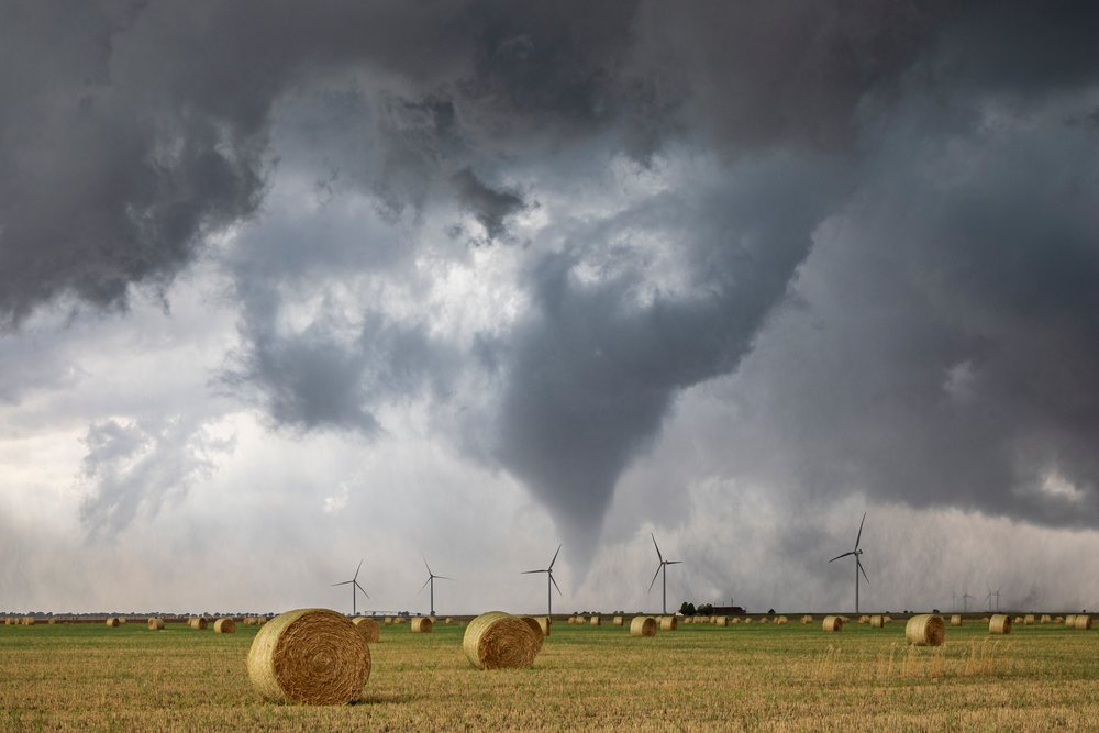 Tornado touching down in a New Mexico field scattered with cut hay and hay bales under storm clouds with wind turbines in the background, Lingo, USA.