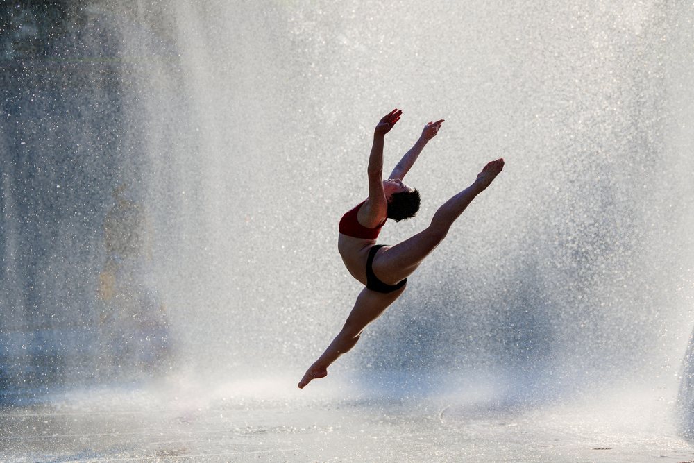Female dancer leaps mid-air through water spray outdoors, USA.