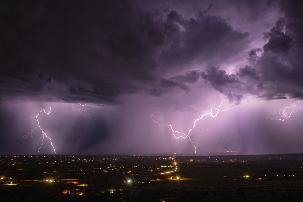 Lightning strikes at night over Sierra Vista near Our Lady of the Sierras during a heavy storm with dark clouds and visible city lights, Storm Chasing, Weather, Environmental Issues, Arizona, USA.