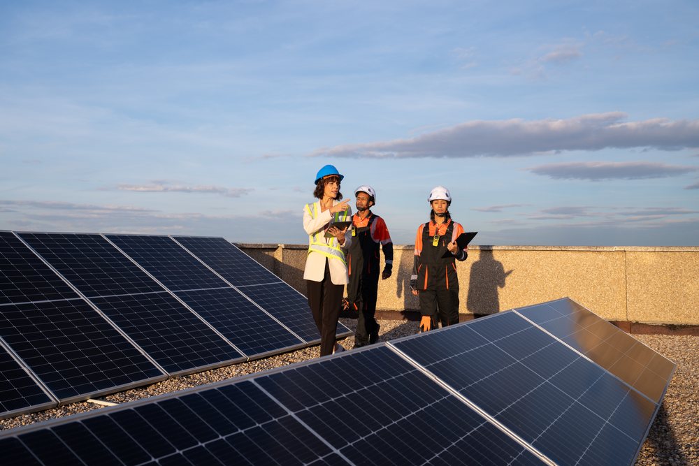 Three engineers inspecting solar panels on a rooftop, Spain under a blue sky with sunlight, Madrid.