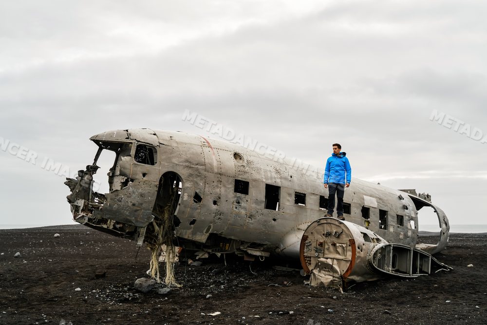 A white person stands on the wreckage of an airplane