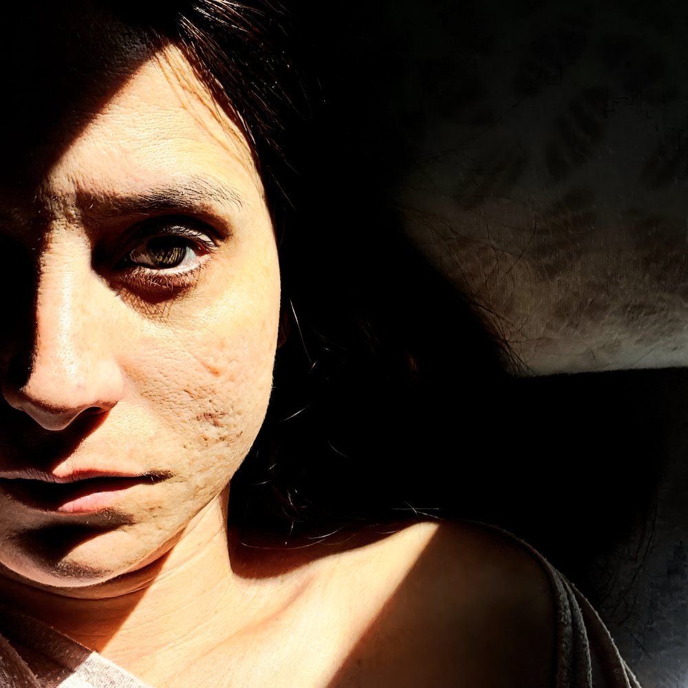 Close-up portrait of a woman with half her face illuminated, showing detailed skin texture and shadow on a dark background, Spain.