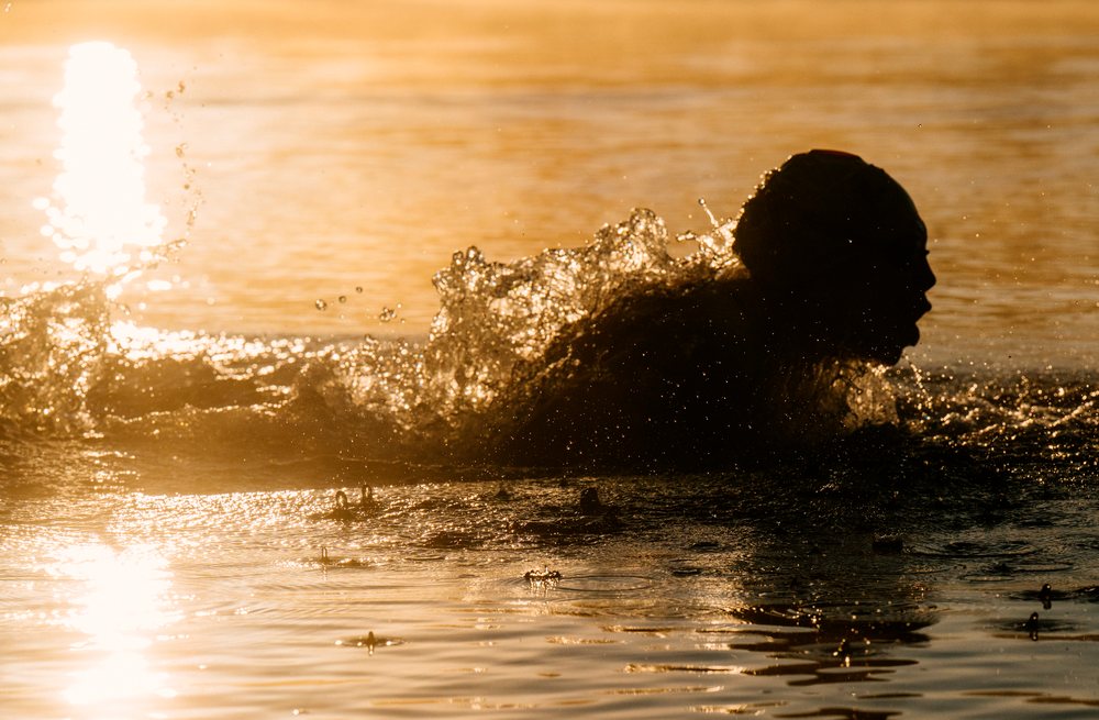Silhouette of a person swimming with splashing water at sunset, USA.