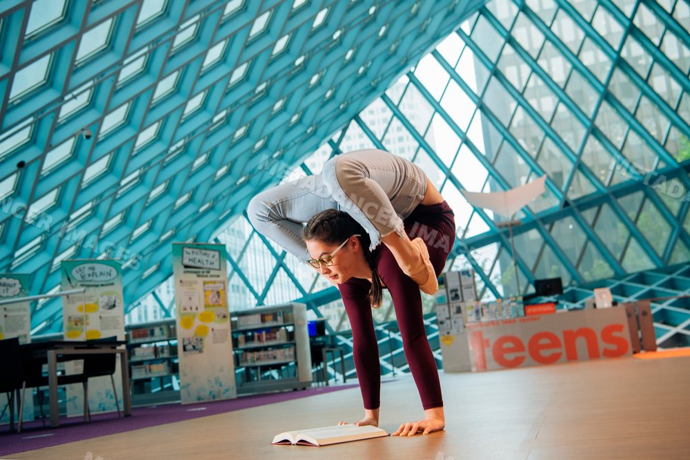 Young woman doing a flexible yoga pose while reading a book