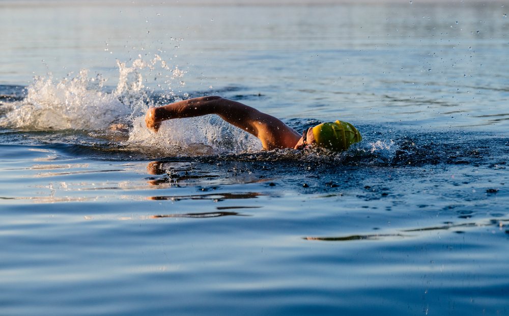 Swimmer performing freestyle stroke in open water with splash, outdoors, USA.