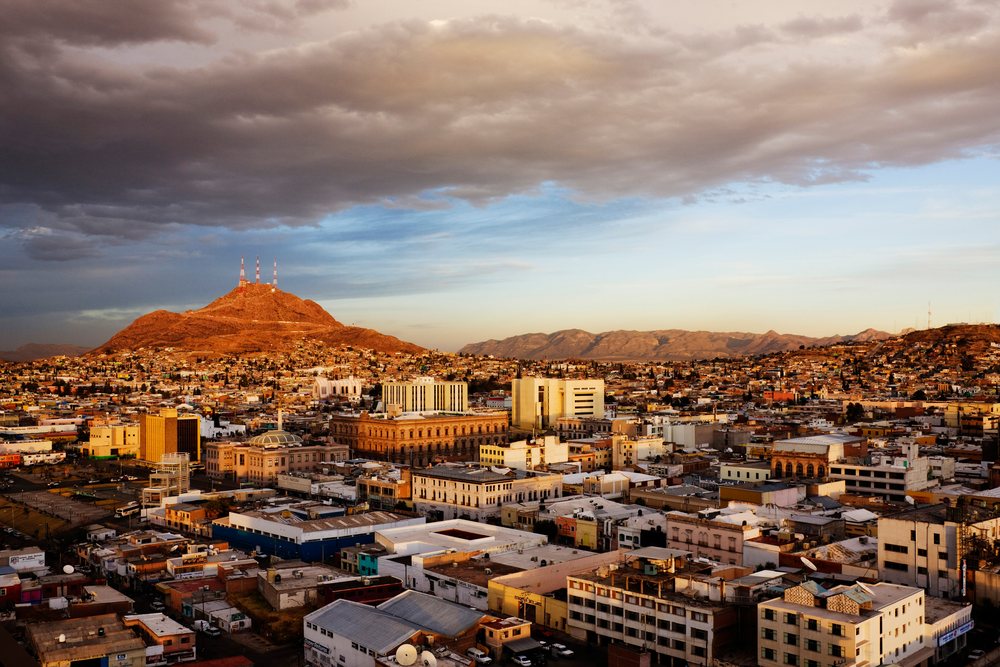 Cityscape of Chihuahua showing various buildings and mountain with television towers under a dramatic sunset sky, Mexico.