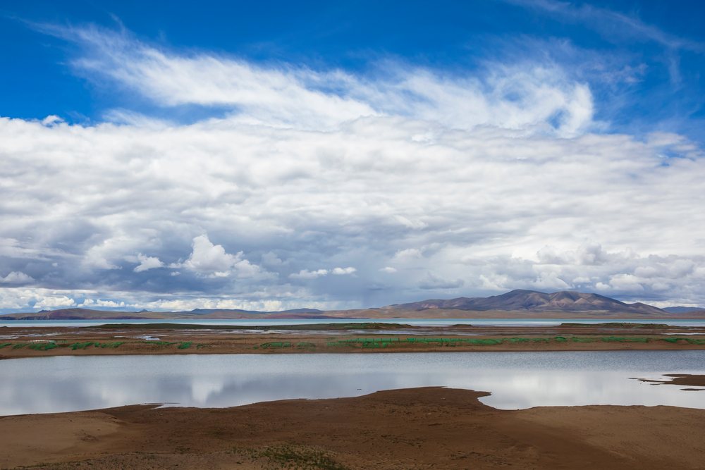 Lake Kuona reflects clouds and distant mountains along the shoreline, Amdo County, Autonomous Region of Tibet.