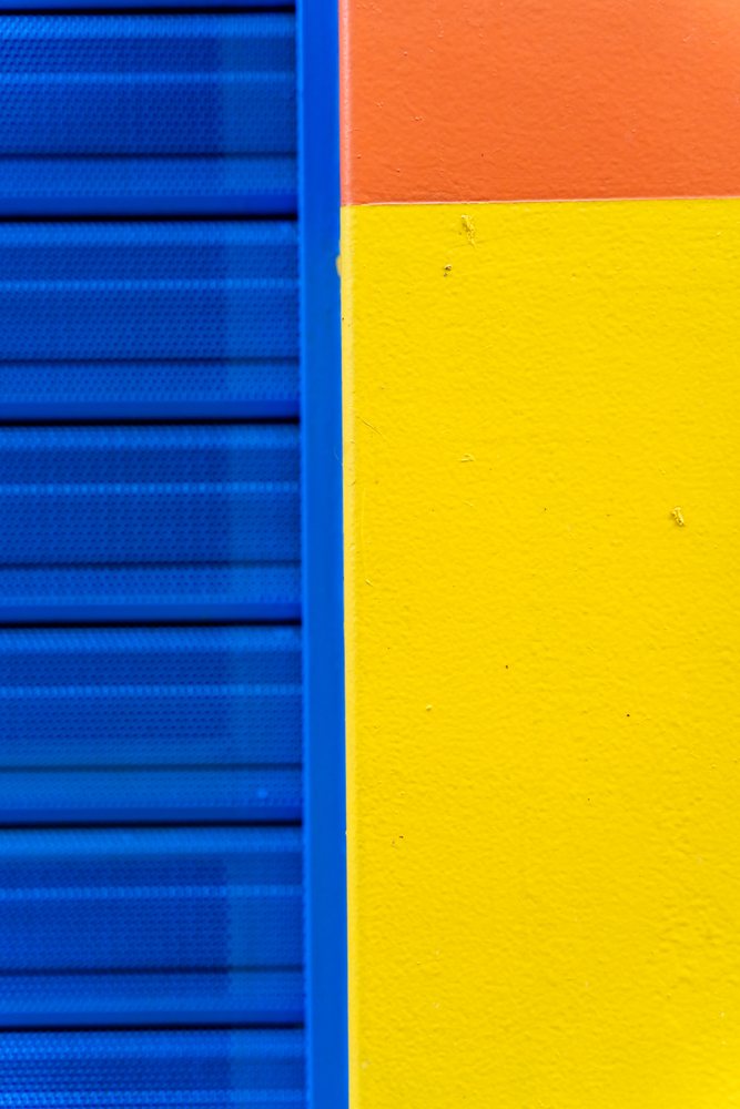 Textured wall corner featuring blue, yellow, and orange painted sections forming a vibrant abstract composition, texture, abstract texture, background, wallpaper, Spain.
