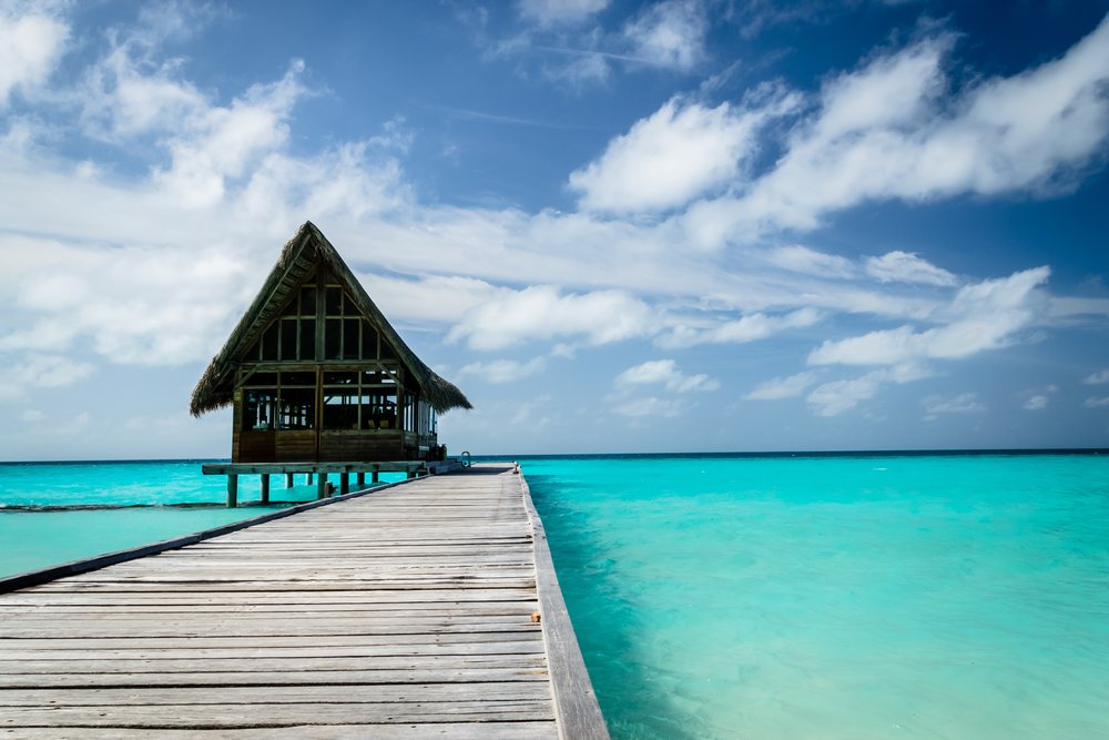 Wooden pier leads to a thatched hut over turquoise tropical ocean water under blue sky with white clouds, summer, Holliday, travel, landscape, Maldives.