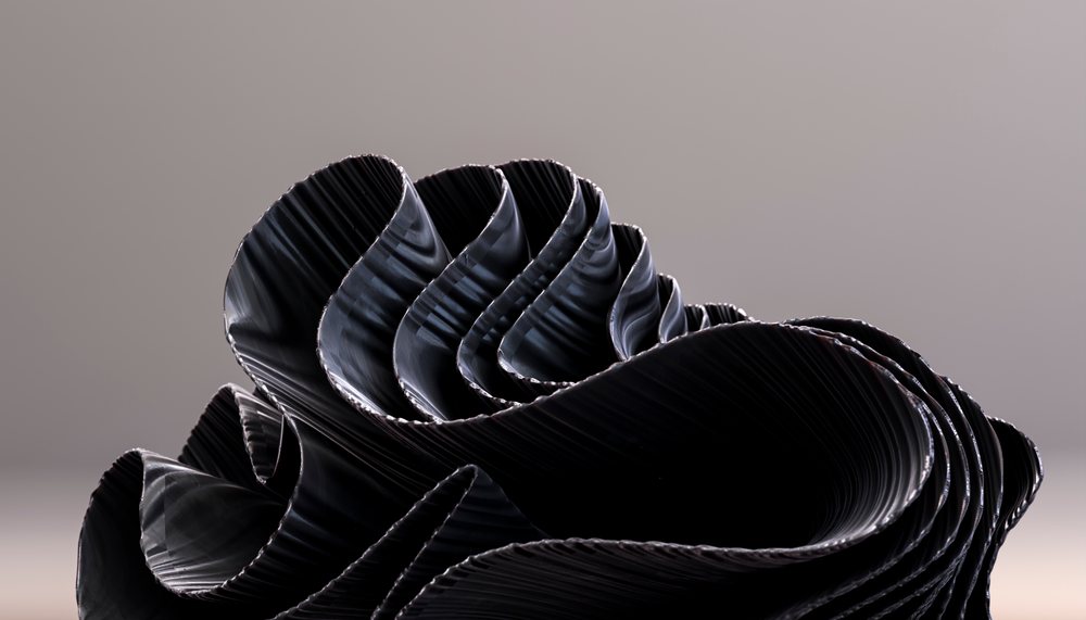 Black sculptural sheets with curved folds and wavy rippled texture form an abstract pattern in a neutral studio setting with soft lighting.
