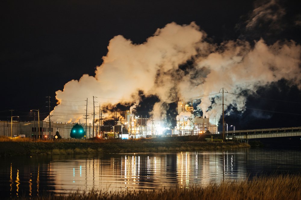 Nighttime view of an industrial plant emitting smoke and steam, with lights reflected on calm water, shington, Tacoma, WA, USA.
