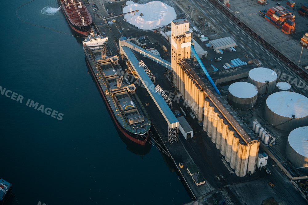 A cargo ship docked at an industrial port next to grain silos in Long