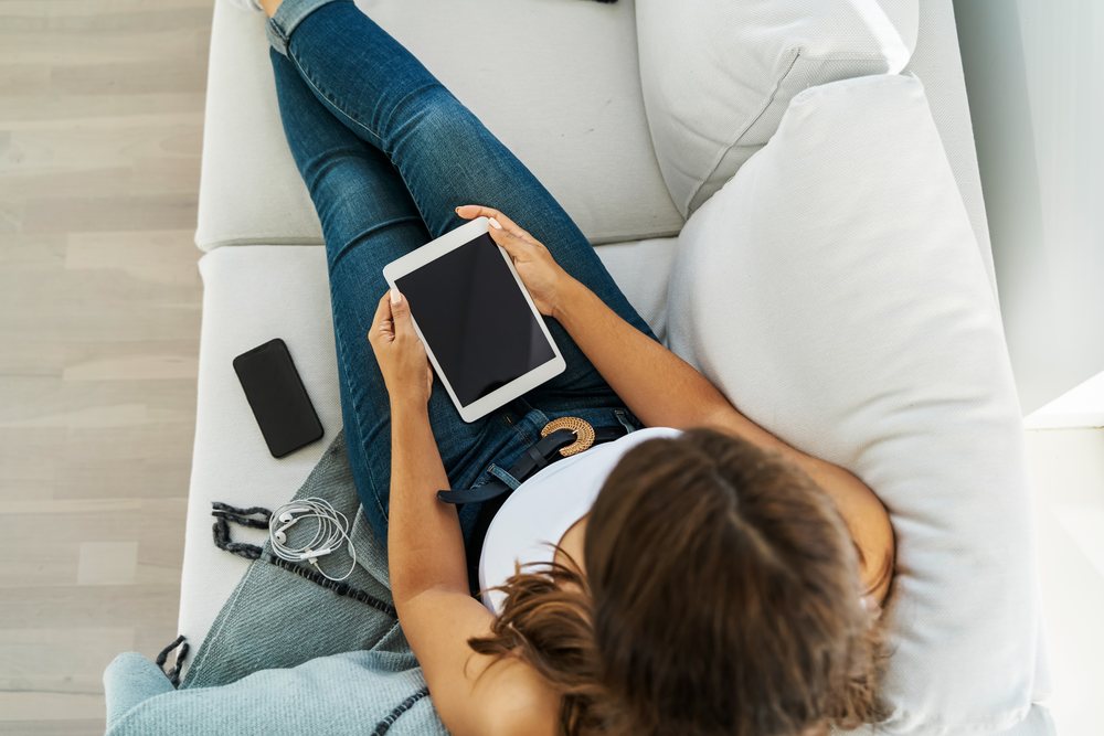 A white woman relaxing on a couch using a tablet