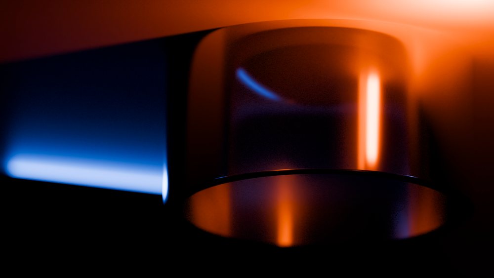 Blue and orange flames burn steadily on a metal gas burner with their light reflecting on its surface in a dark environment.
