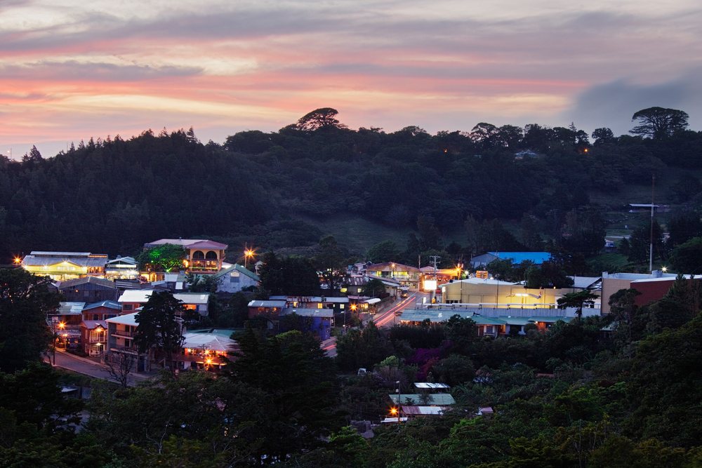 Sunset over Santa Elena village with illuminated buildings and surrounding forested hills in Costa Rica.
