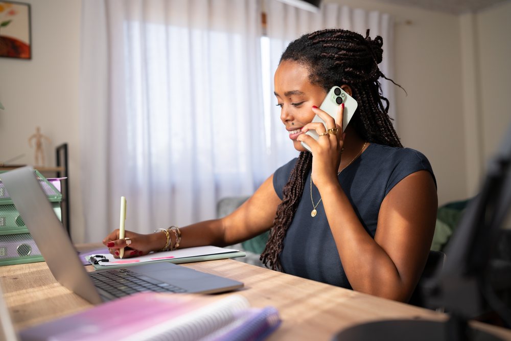A woman is working and taking notes while talking on the phone in a home office setting, remote work, student, Spain.