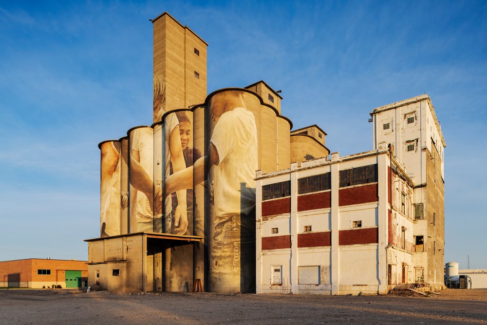 Large Grain Silo, decorated with a mural by Australian artist Guido Van Helten in an industrial setting under clear blue sky, Weather, Environmental Issues, Storm Chasing, Salina, Kansas, USA.