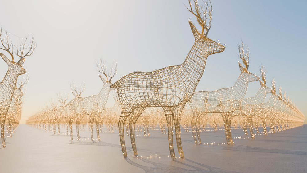 Wireframe reindeer sculptures decorated with string lights arranged in rows in an outdoor setting during the daytime.