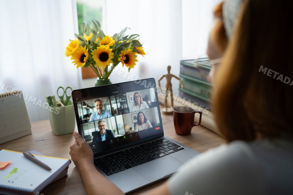 A white woman telecommutes with colleagues on a video call