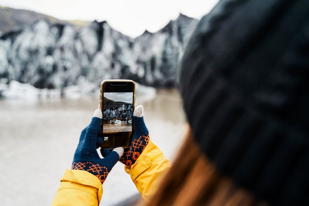 A white person captures a photo of an icy glacier landscape