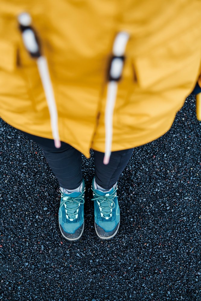 A white person wearing hiking boots stands on black pebbles
