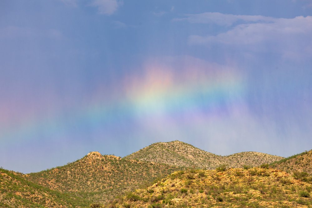 Rainbow arcs over hilly desert terrain during a mid-afternoon rainstorm, Storm Chasing, Weather, Environment, Tombstone, Arizona, USA.